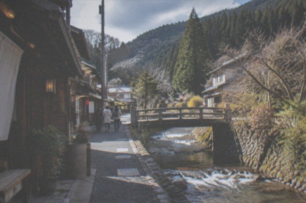 Mountain village street beside a stream with cedar forest slopes behind