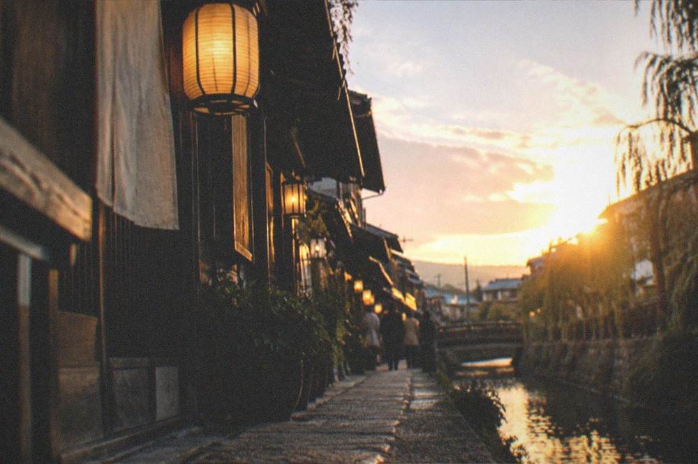 Lantern-lit narrow alley beside a canal in central Kyoto at dusk