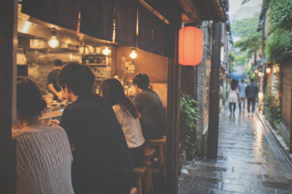People drinking and eating at a busy izakaya counter in Kyoto in the evening