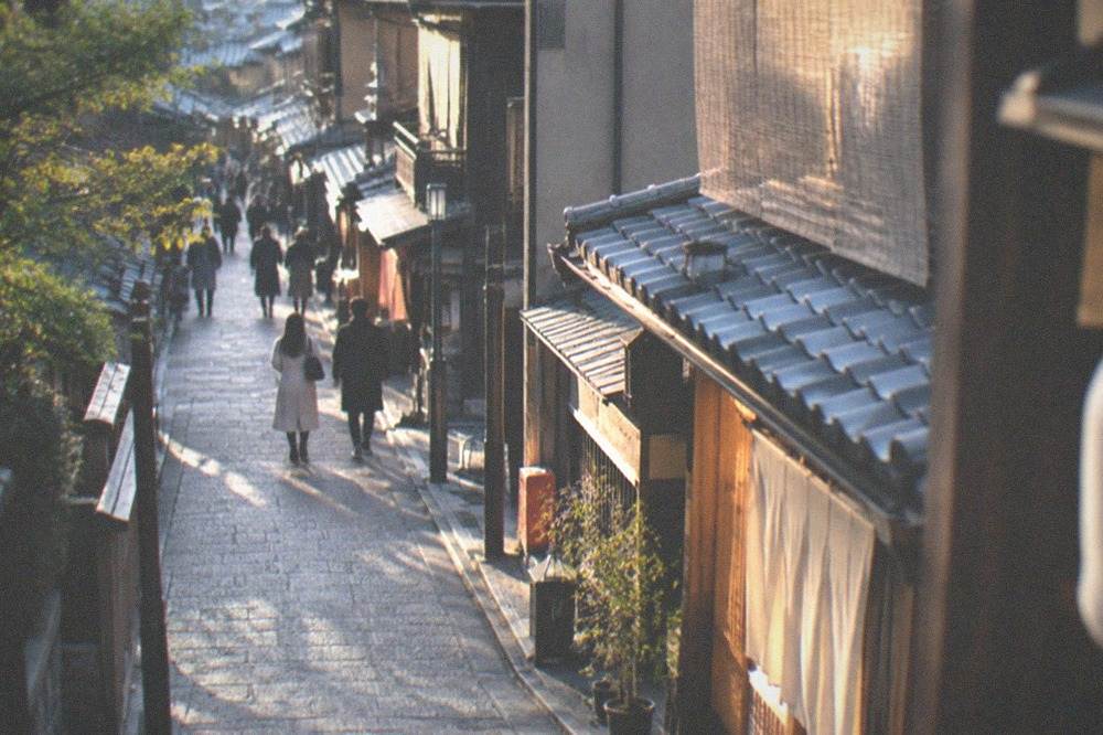 A maiko or geiko walking quickly along a darkened wooden street in Gion, seen from a distance