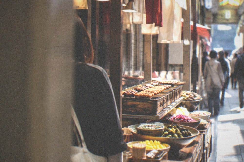 Food stalls with grilled skewers and pickles under the covered arcade of Nishiki Market