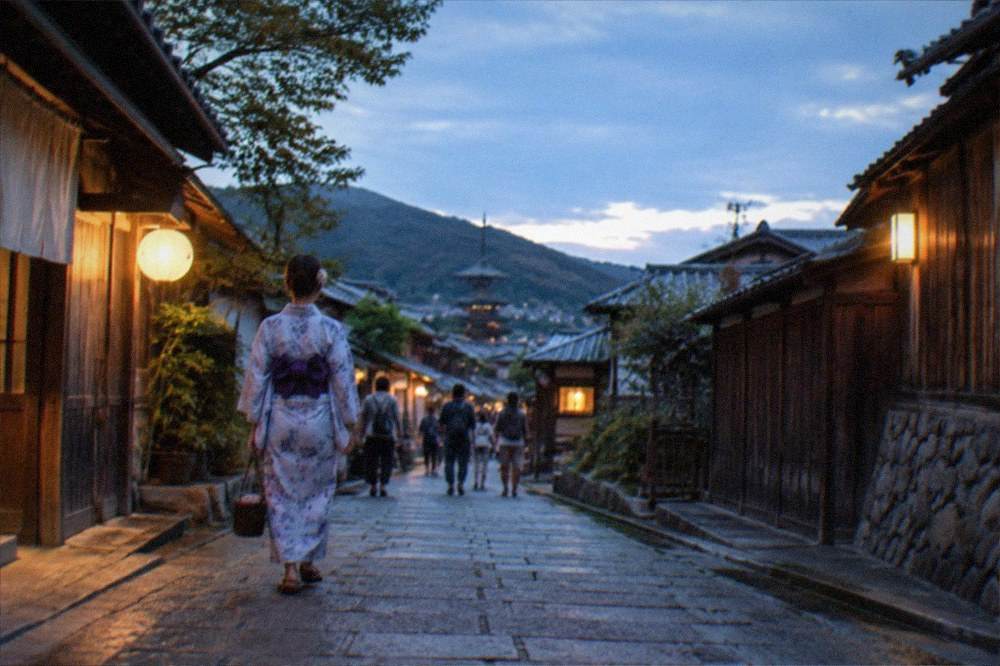 A woman in a yukata walking a stone lane between wooden buildings in a mountain village