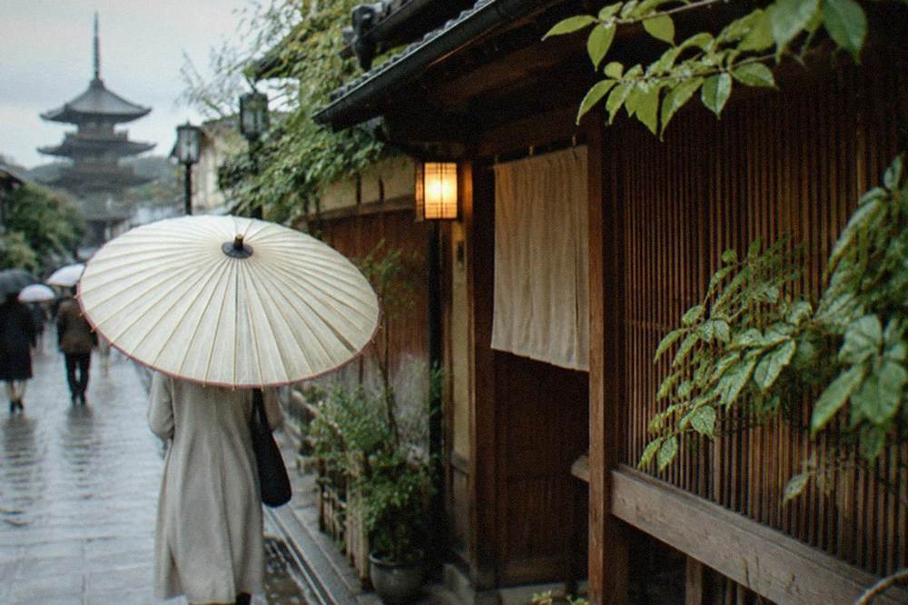 A large paper umbrella held over a puddled lane beside a wooden teahouse in Kyoto
