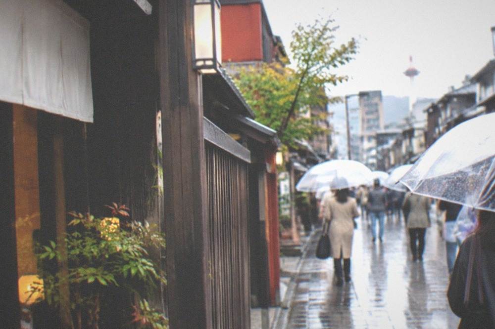 Clear plastic umbrellas moving along a wet shopping arcade street in Kyoto