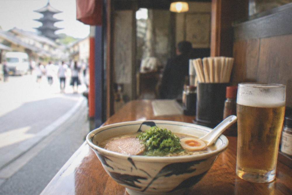 A bowl of ramen and a beer on a wooden counter in a small izakaya