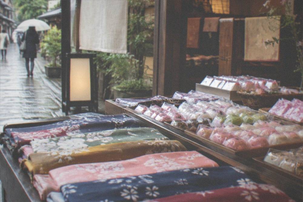 A display of folded fabric goods and small wrapped sweets inside a Kyoto shop