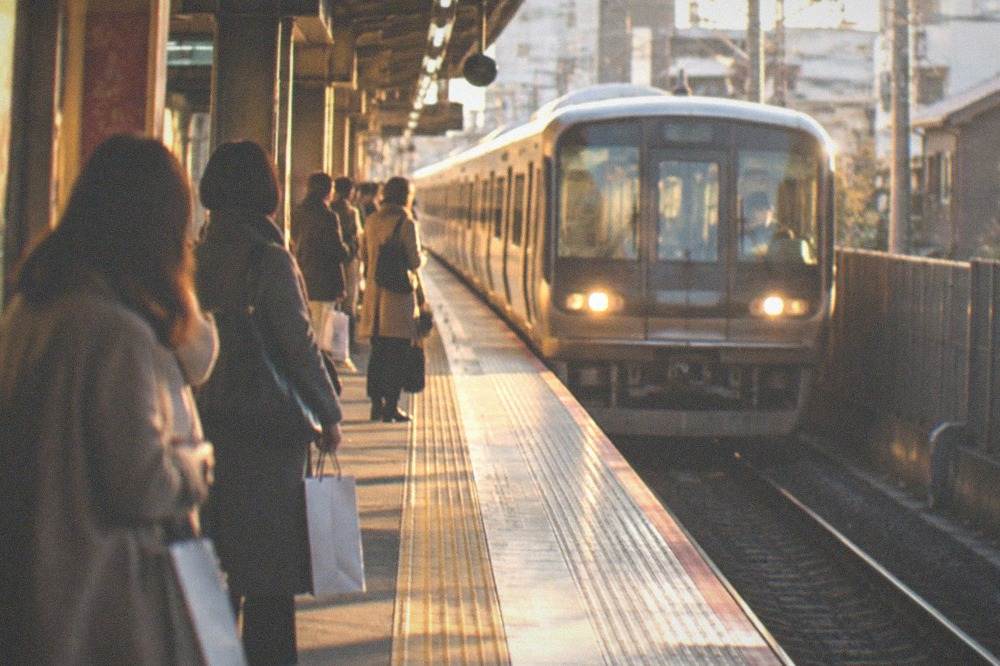 A subway station platform in Kyoto with a train arriving and passengers waiting with shopping bags