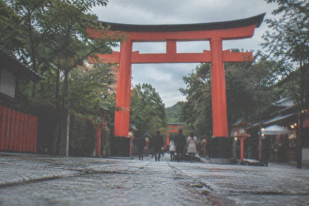 A tall vermillion torii gate rising over a tree-lined avenue in Kyoto