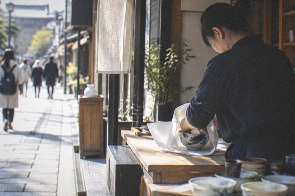 A shopkeeper wrapping a purchased ceramic bowl in paper at a counter