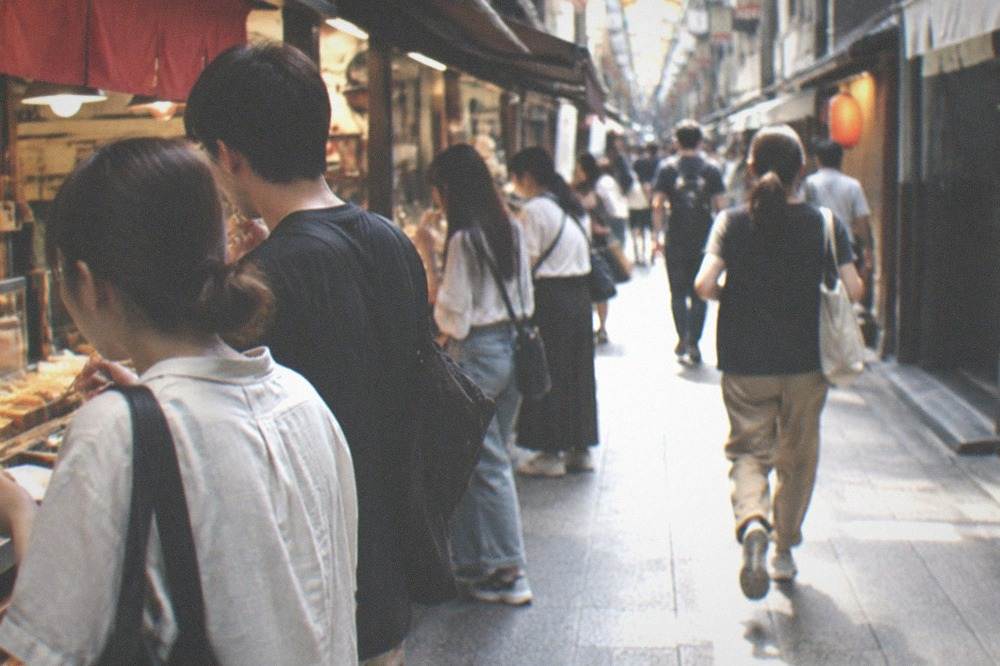 Customers standing at a food counter eating small snacks in a narrow market lane