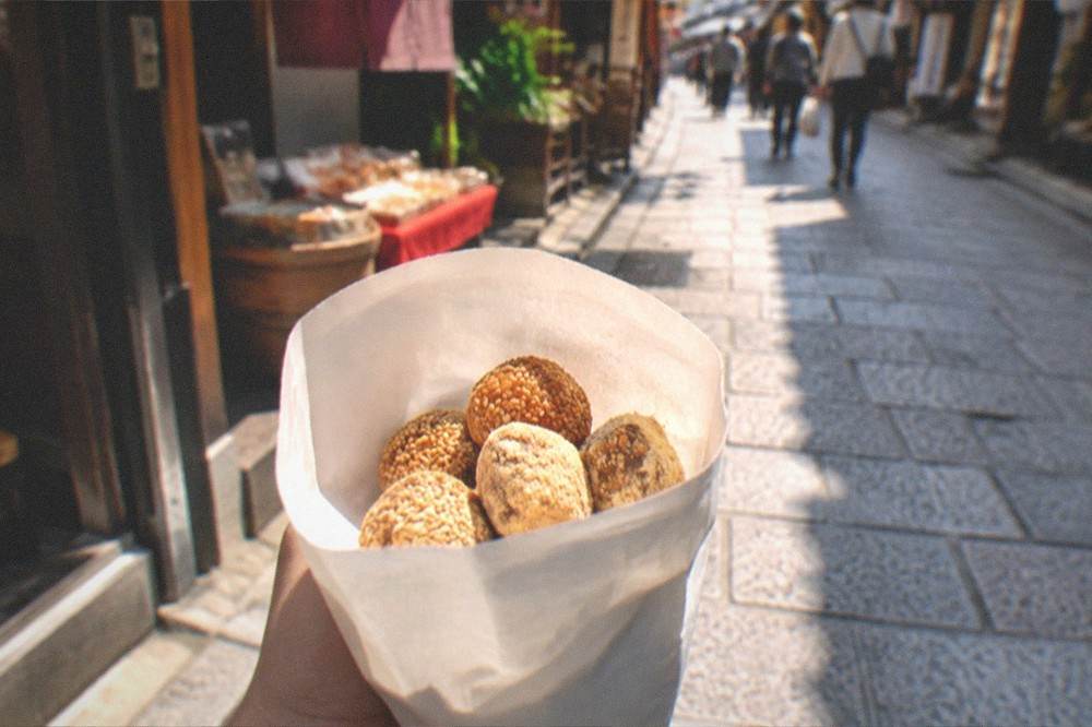 A paper bag of sweet snacks held in hand above a stone paved street