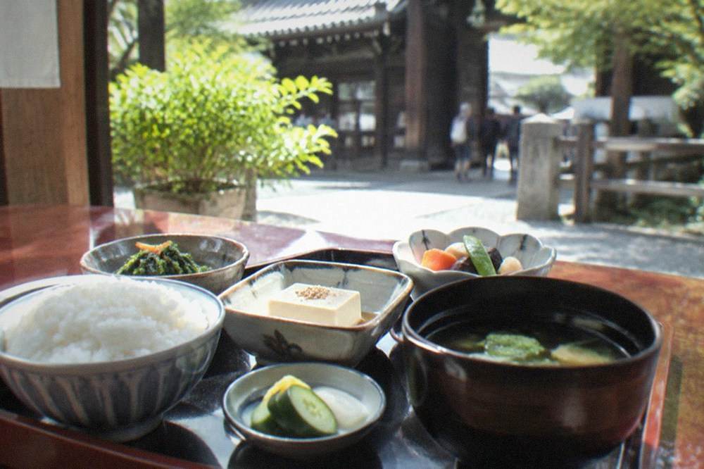 A shojin ryori tray with small dishes of vegetables, sesame tofu and rice on a lacquered table