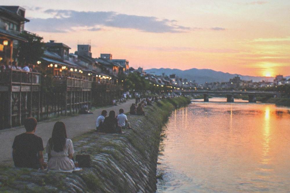 The Kamo River in Kyoto at dusk with couples and diners seated along the bank