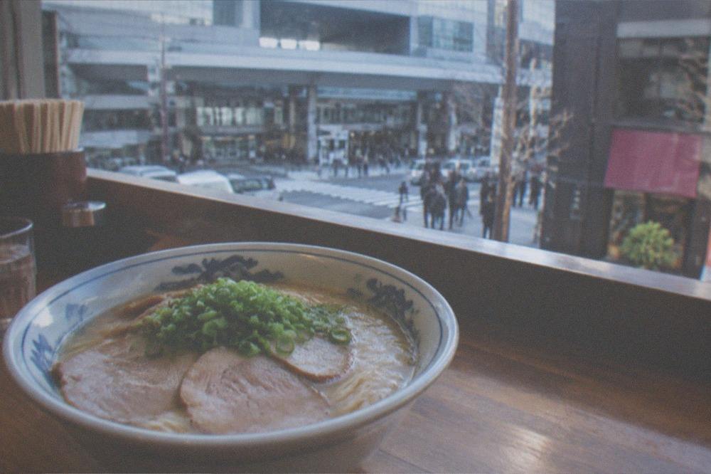 A bowl of ramen with sliced pork and green onion on a wooden counter