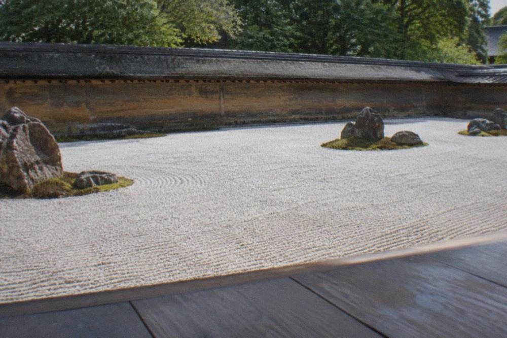 A raked white gravel zen garden with dark rocks arranged in clusters, viewed from a wooden temple veranda