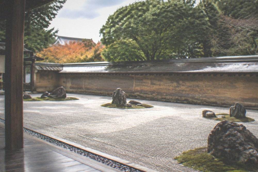 A moss carpet broken by upright stones, viewed from a low temple veranda under soft light