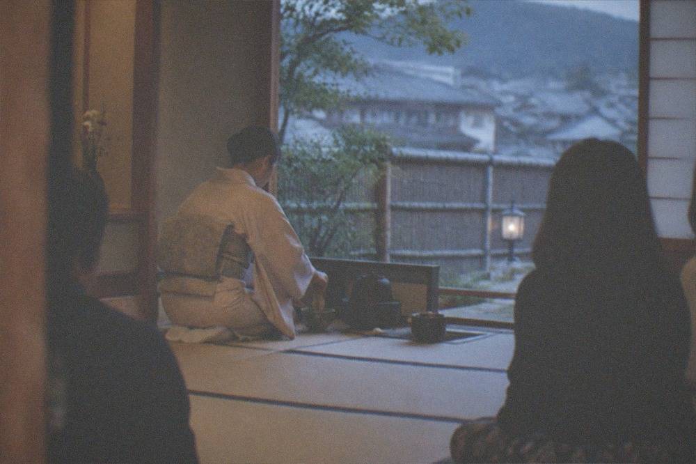 A host whisking matcha in a tatami room while guests sit on cushions