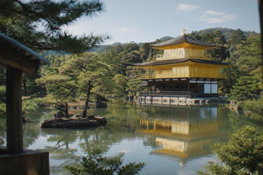 The golden pavilion of Kinkaku-ji reflected in the pond in front of it, with pine trees around the water