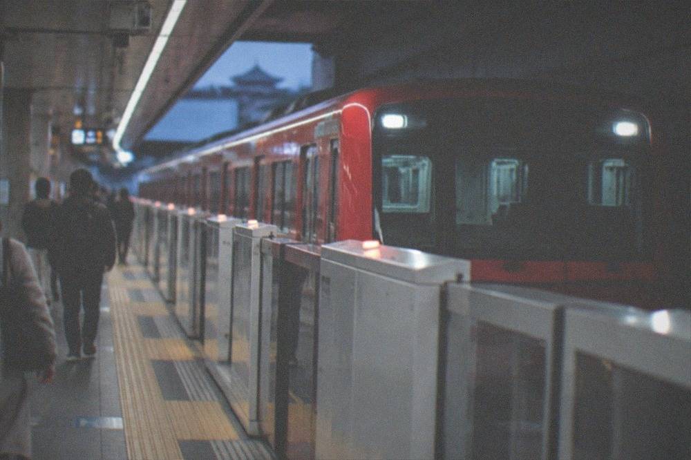 A red city subway train pulling into an underground platform with platform screen doors