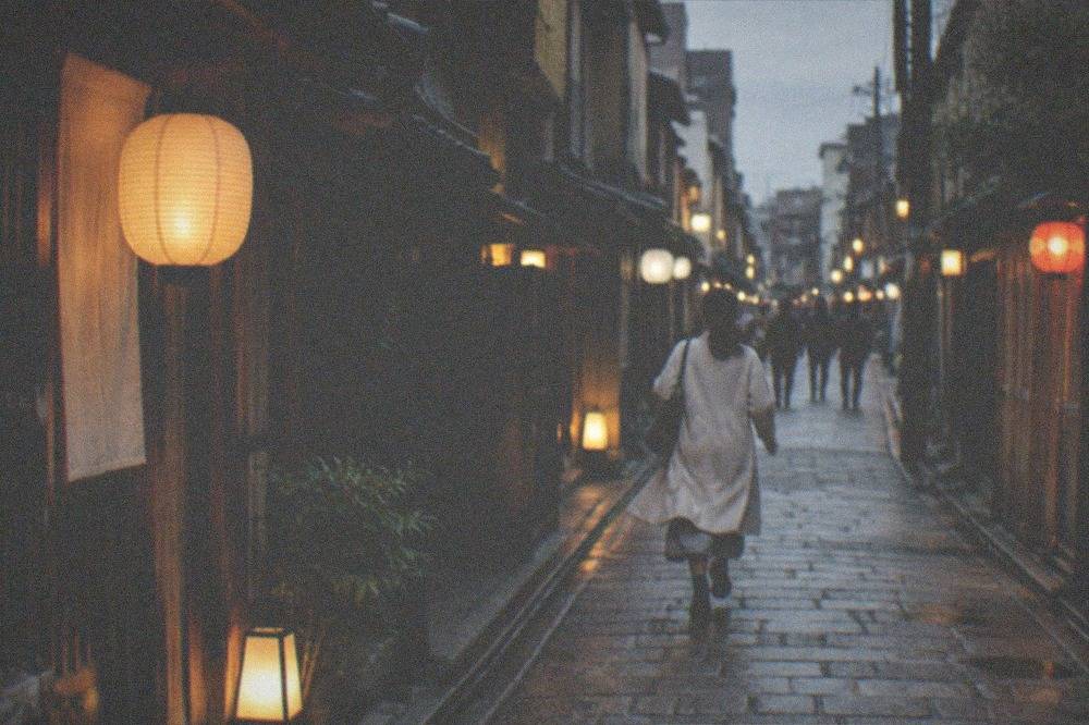 A stone-paved lane with wooden facades and hanging lanterns at night
