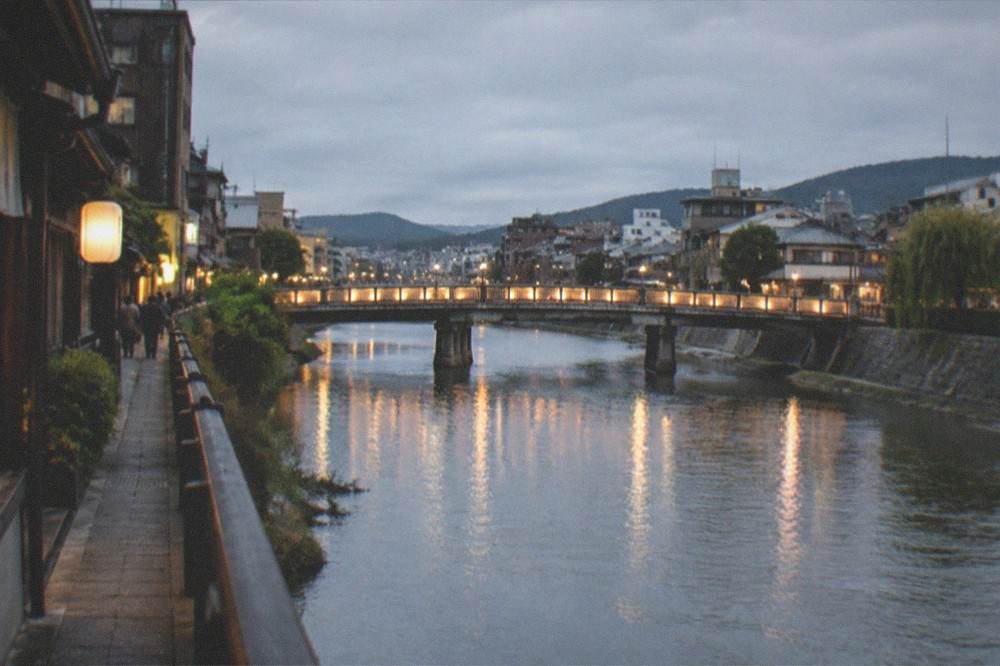 A lit bridge over a river with city lights reflected in the water