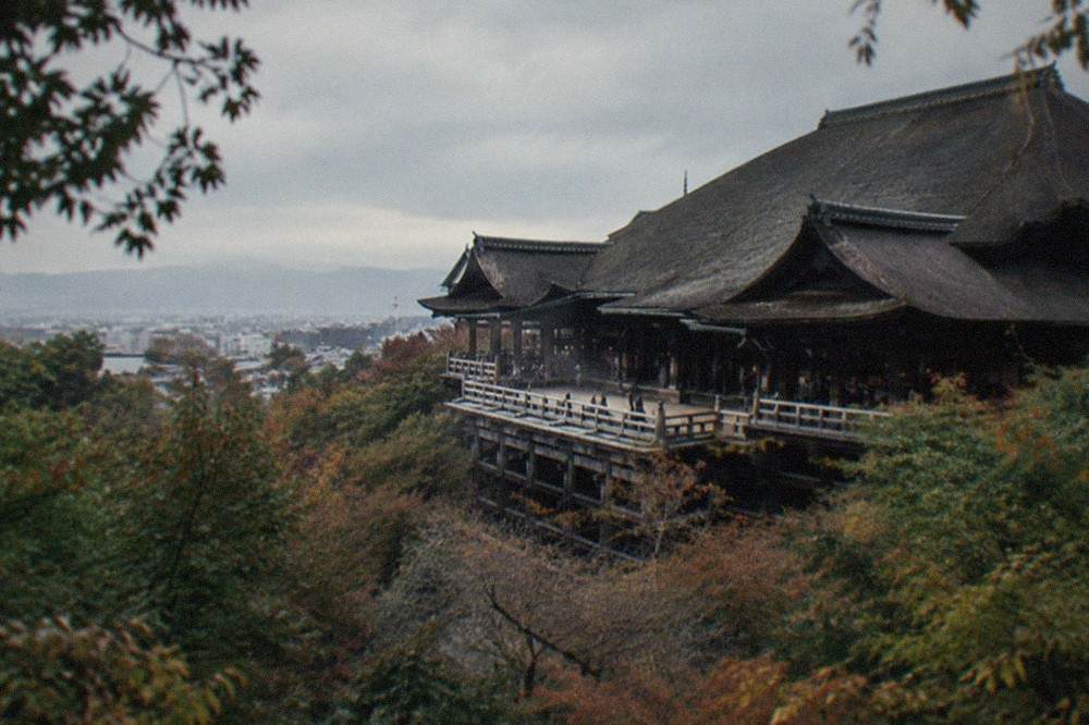 Kiyomizu-dera's wooden stage seen from the wooded hillside below in the late afternoon