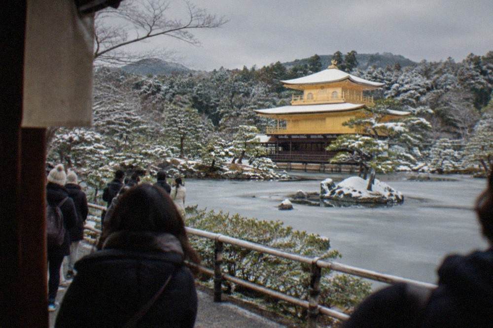 The golden pavilion of Kinkaku-ji seen across a frozen pond with snow on the surrounding pines