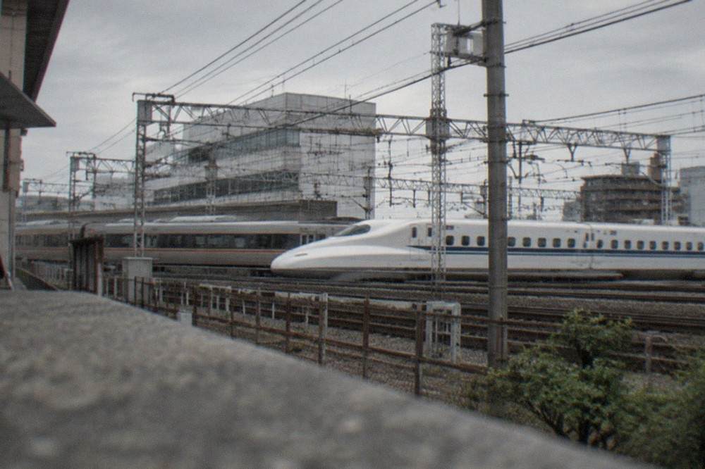 A shinkansen and express train passing on railway tracks outside a Japanese station at midday