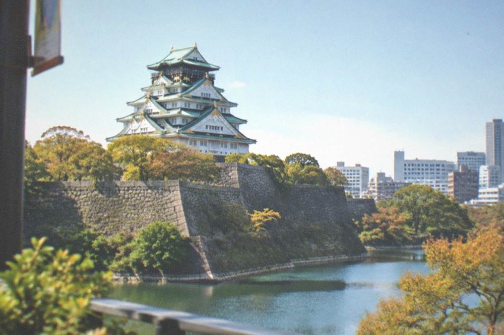 Osaka Castle keep rising above its stone walls and moat, with the modern city skyline behind it