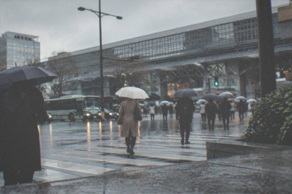 Commuters with umbrellas crossing a street near Kyoto Station in rain